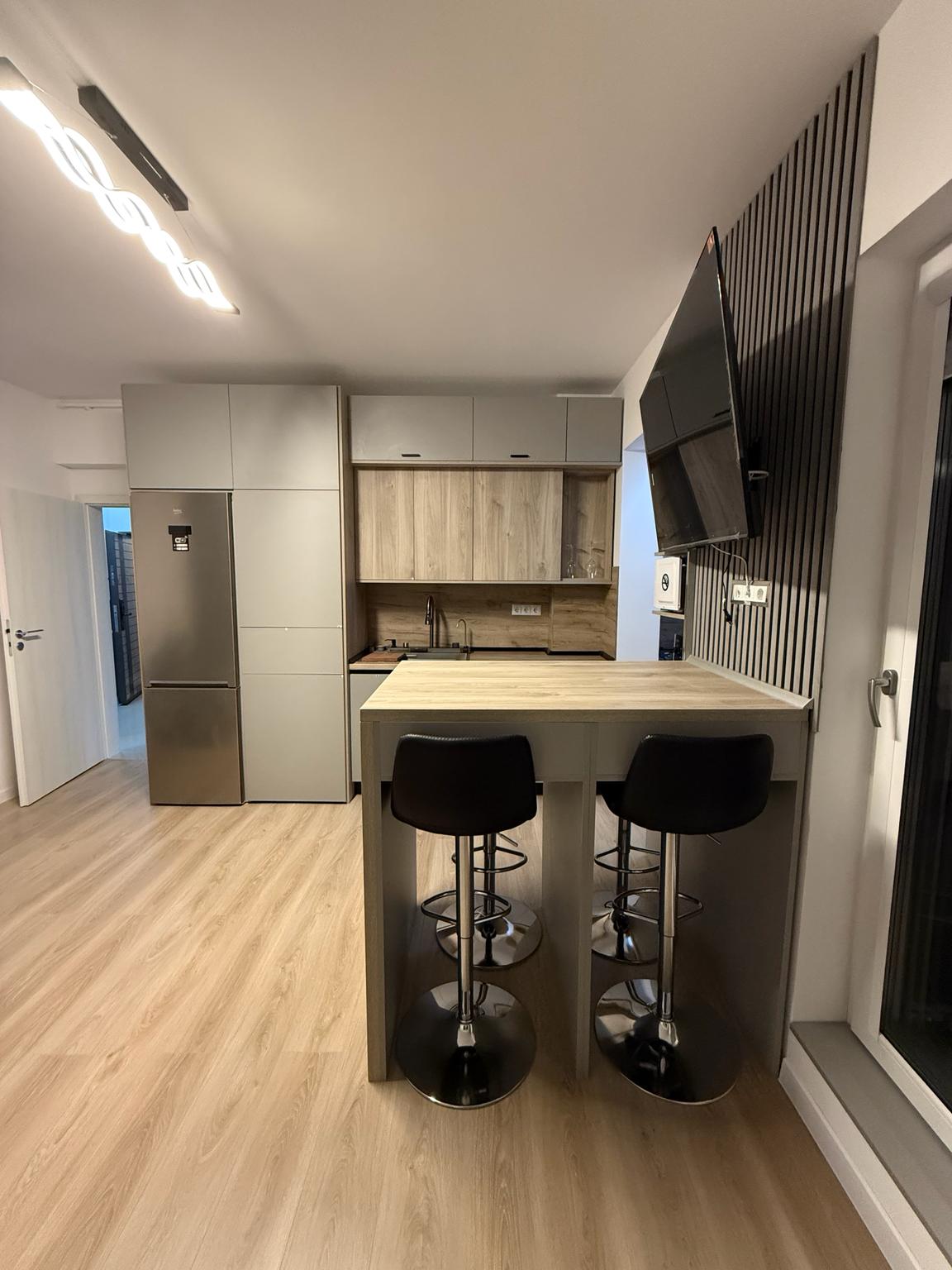 Bucătărie cu mobilier gri, blat cu aspect de lemn și masă integrată